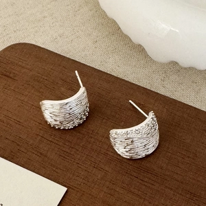 Détail de boucles d'oreilles en C argentées texturées avec zircons sur support en bois