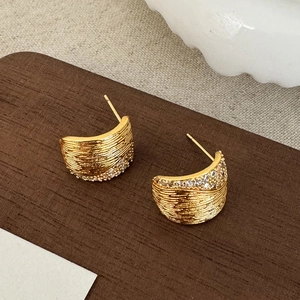 Gros plan de boucles d'oreilles dorées texturées avec zircons sur une surface en bois