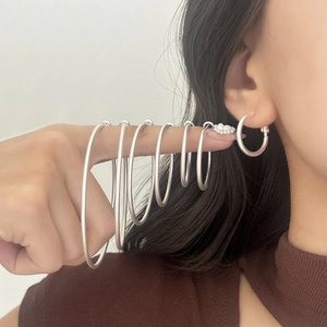 Macro shot of 6 different sized matte silver hoop earrings held on a finger for size comparison