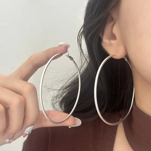 Detail view of large matte silver hoop earrings worn by a model to show scale and style