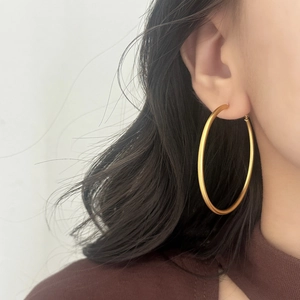 Close-up of a large gold hoop earring with a satin matte finish worn by a model