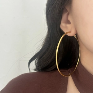 Macro detail of large matte gold hoop earrings showing brushed metal texture on a model