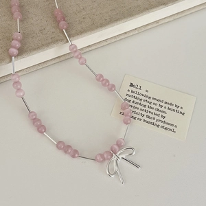 Vue détaillée du collier en œil de chat rose avec pendentif nœud argenté et tubes en métal
