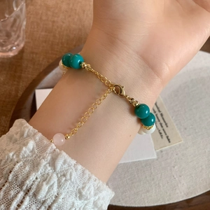 Elegant gold beaded bracelet with green and pink natural stones on female wrist