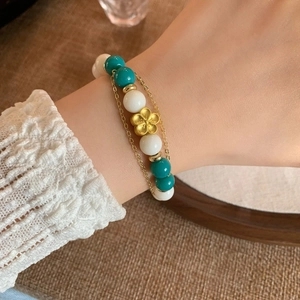 Handmade beaded bracelet with turquoise stones and matte gold flower charm on wrist