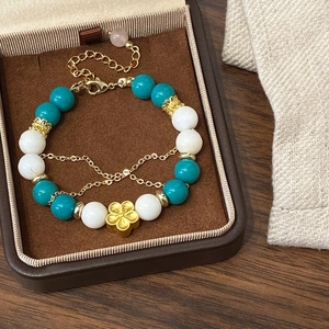 Elegant beaded bracelet with blue and white stones featuring a gold flower charm in a box
