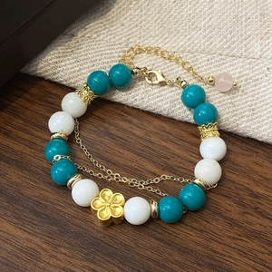 Detail of beaded bracelet with turquoise stones and golden flower pendant on linen