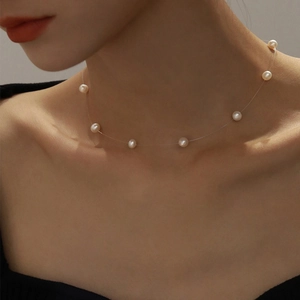 Detail view of small white pearls on a transparent invisible line necklace on a model