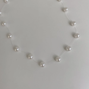 Detailed view of elegant white pearl necklace on invisible transparent fishing line cord