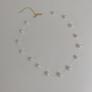 Detail view of round white pearls on invisible cord with gold adjustable clasp and chain