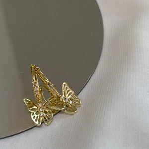 Boucles d'oreilles créoles papillon dorées avec zircons montrées dans un reflet miroir
