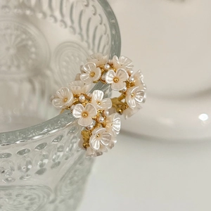 Elegant gold flower cluster earrings with white petals and pearls on a glass rim