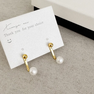 Detail of J-shaped gold plated earrings featuring round white freshwater pearls