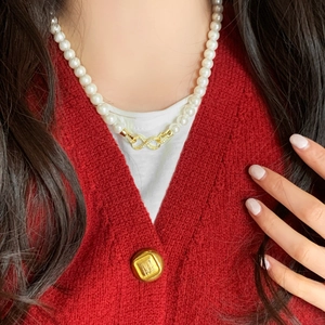 Elegant pearl necklace with gold infinity symbol worn by model over a red cardigan