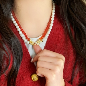 Double-layered necklace with white pearls and red agate beads featuring a gold infinity clasp