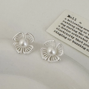 Dettaglio orecchini a fiore traforati in argento con perle su sfondo vintage