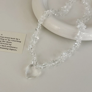 Close-up of heart pendant and transparent white crystal stone necklace on white surface