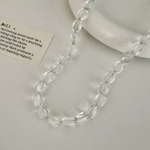 Detail shot of minimalist transparent glass bead necklace on a creamy beige surface