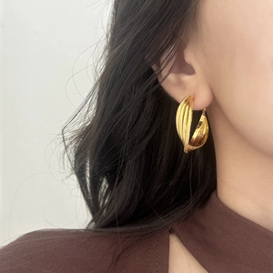 Close-up of golden Mobius hoop earrings with polished and frosted layered metal design