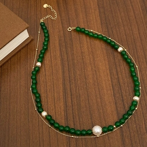 Detailed view of emerald green chalcedony and white pearl necklace on dark wood surface