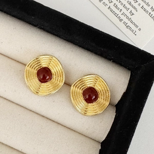 Detail of vintage gold ripple earrings with dark red stones on a velvet tray