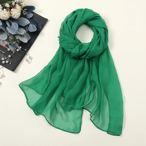 Flat lay of an emerald green lightweight chiffon scarf with elegant pearl accessories