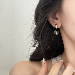Elegant gold heart earrings with transparent glass pendants worn on a model ear