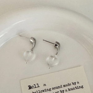 Detailed view of heart-shaped glass earrings with silver hooks on a ceramic tray