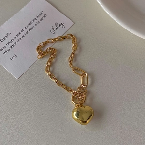 Golden heart pendant bracelet with chunky chain and OT buckle on textured background