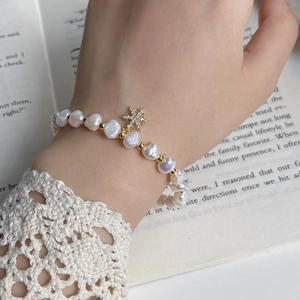Detail of freshwater baroque pearl bracelet with gold snowflake charm on lace sleeve