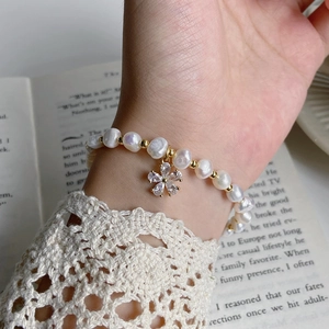Baroque freshwater pearl bracelet with a sparkling gold flower pendant worn on a wrist