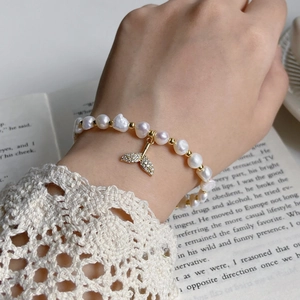 Close-up of freshwater pearl bracelet with golden fishtail pendant on lace sleeve