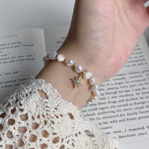 Close-up of Baroque pearl bracelet featuring a gold starburst pendant on a lace sleeve