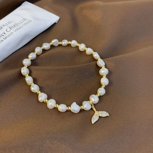 Detailed close-up of a freshwater pearl bracelet with a sparkling gold whale tail charm