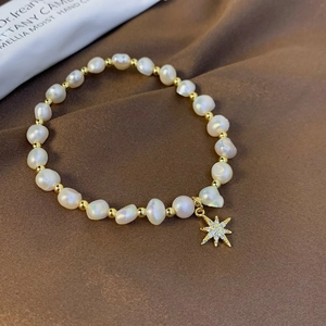 Close-up of freshwater pearl bracelet with a sparkling gold star pendant on silk