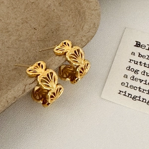 Detailed view of gold hollow fan-shaped earrings on textured brown paper backdrop