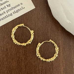 Close-up of golden irregular lava texture hoop earrings on a vintage wooden background