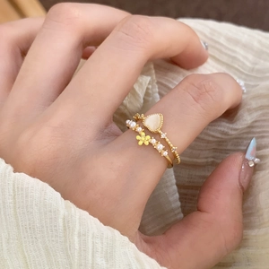 Detail of stacked gold rings with heart-shaped white stone and small pearl floral band