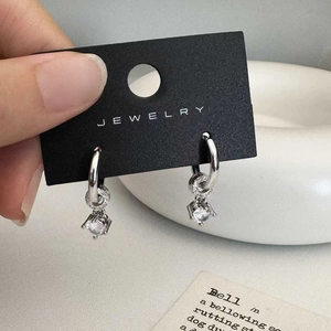 Close-up of elegant silver zircon earrings with four-prong setting on jewelry card