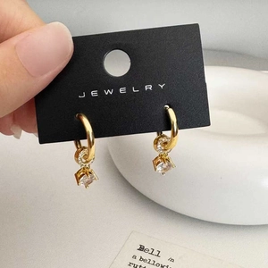 Close-up of gold dangle earrings with small hoop and square claw-set zircon stone