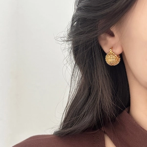 Detailed close-up of golden hollow mesh woven spherical earrings worn by a model