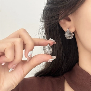 Detail view of silver hollow woven ball earrings with intricate mesh metallic texture