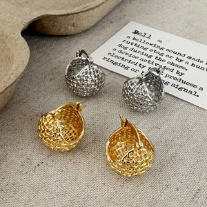Detail of gold and silver woven mesh earrings on a minimalist textured fabric background