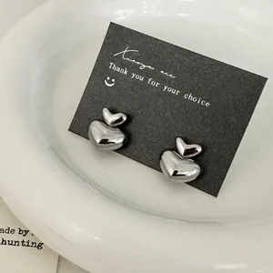Minimalist double heart silver studs displayed on black card in a white ceramic dish