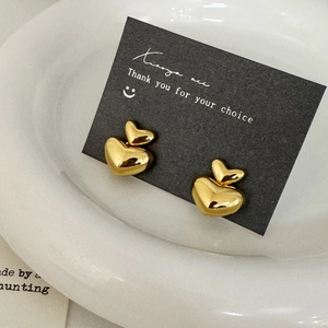 Polished gold double heart stud earrings on a premium black and white display stand