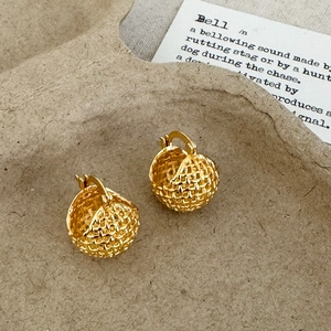 Detail of golden woven spherical earrings featuring textured mesh design on a natural tray