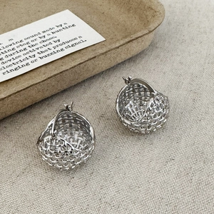 Detail of silver grid ball earrings with a unique woven basket design on a rustic background