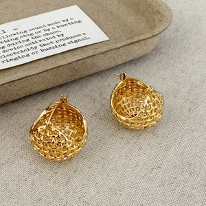 Detail of gold woven mesh hoop earrings on a vintage card and rustic fabric background