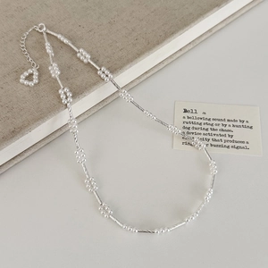 Detail van gedraaide zilveren ketting met witte parels en hartvormige parelhanger