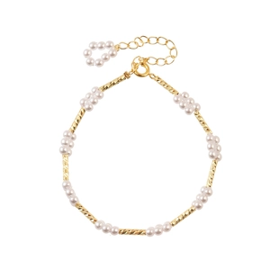 Detail van goudkleurige metalen buisjes en witte parelclusters op de elegante ketting